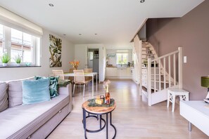Una sala de estar moderna con un sofá, una mesa de comedor y sillas. Se ve una escalera que sube a otro nivel.