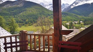 A wooden deck with a view of a mountainous landscape, including snow-capped peaks and a valley with greenery and buildings.