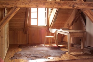 Una habitación de madera con techo inclinado, un escritorio, una silla y una alfombra de piel grande en el suelo.