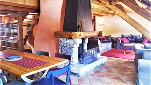 A rustic interior with a stone fireplace, wooden beams, a wooden table, and a sofa area.