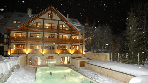 A multi-story lodge with a pool area, surrounded by snow.