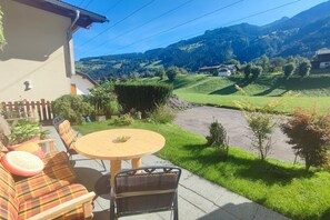 Uma área externa com mesas e cadeiras, um sofá e vista para uma paisagem montanhosa.