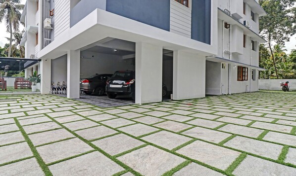 Un edificio moderno con estacionamiento cubierto, un sendero pavimentado y una pequeña zona de estar al aire libre.