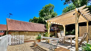 Un espace patio agrémenté d’une pergola, de sièges et d’un bâtiment en pierre en arrière-plan.