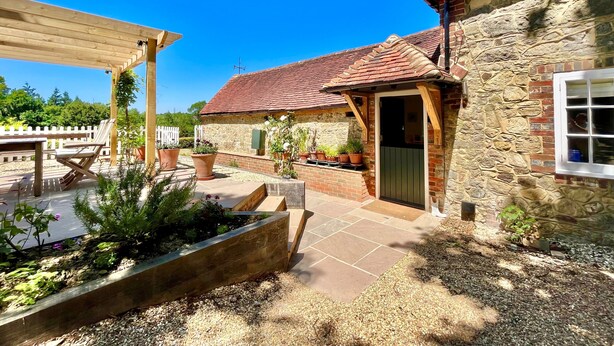 A stone building with a tiled roof, a wooden pergola, and a garden area with potted plants. - The Old Stables by Inspire Stays dot com - a cottage that sleeps 4 guests  in 2 bedrooms (Near Petworth)