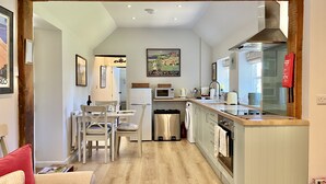 A modern kitchen with a wooden beam ceiling, a dining area with a table and chairs, and a kitchen counter with appliances. - The Old Stables by Inspire Stays dot com - a cottage that sleeps 4 guests  in 2 bedrooms (Near Petworth)