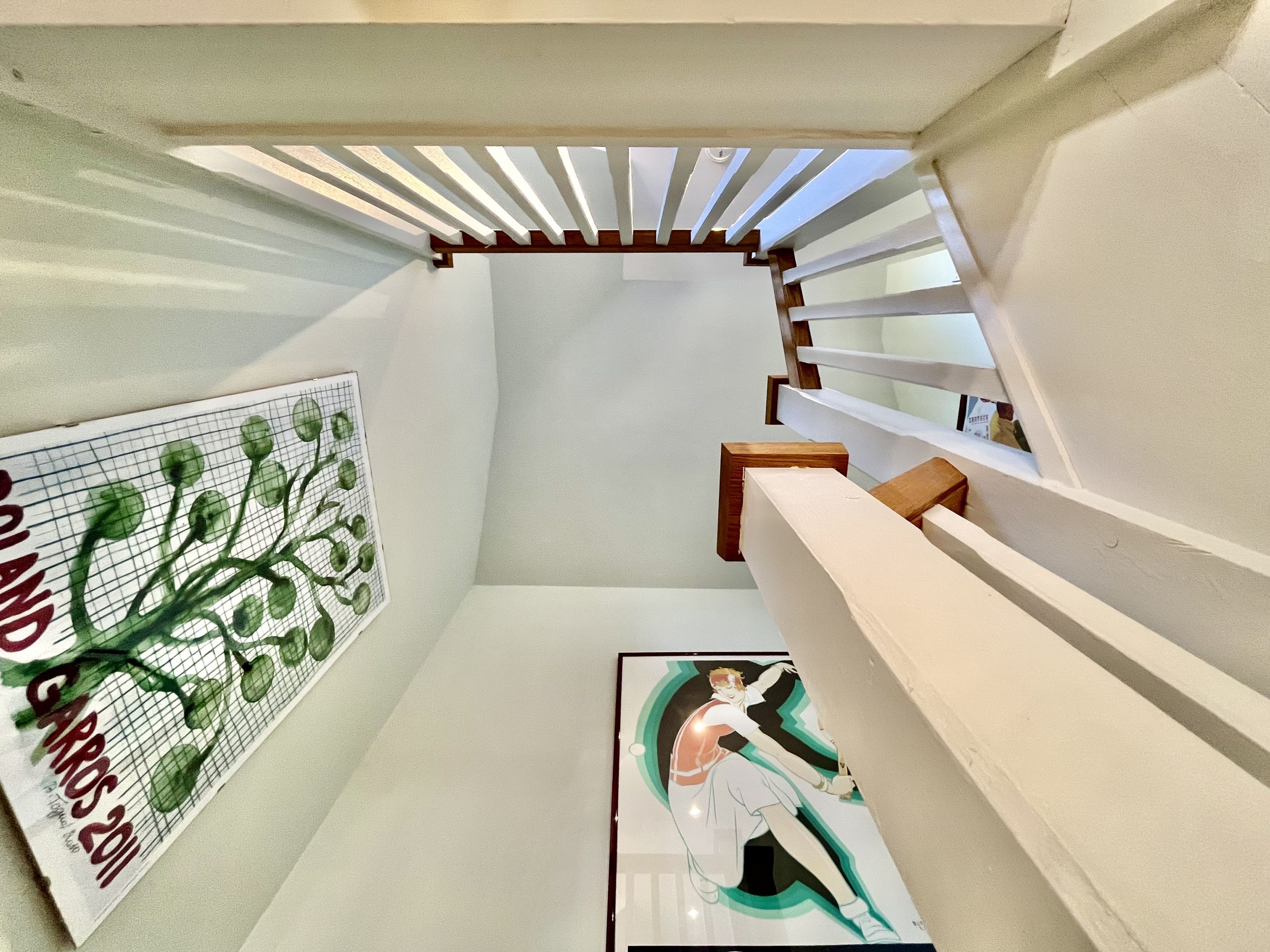 Un escalier moderne et étroit, doté de rampes blanches et d’une main courante en bois.