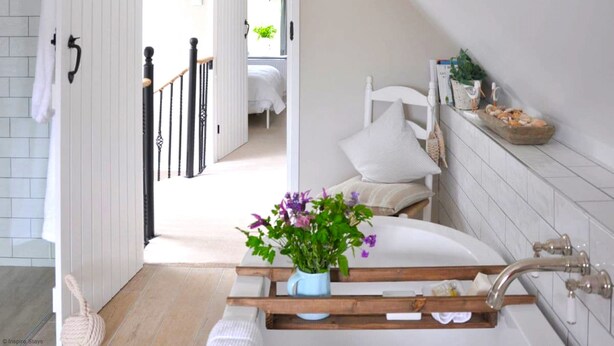 A bathroom with a bathtub, a wooden shelf with toiletries, and a view into the bedroom. - Mill Barn by inspirestays.com - a cottage that sleeps 2 guests in 1 bedroom (North Chailey)
