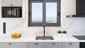 Une cuisine moderne dotée d’un four à micro-ondes encastré, d’un évier à deux bacs et offrant une vue sur la mer grâce à une grande fenêtre.