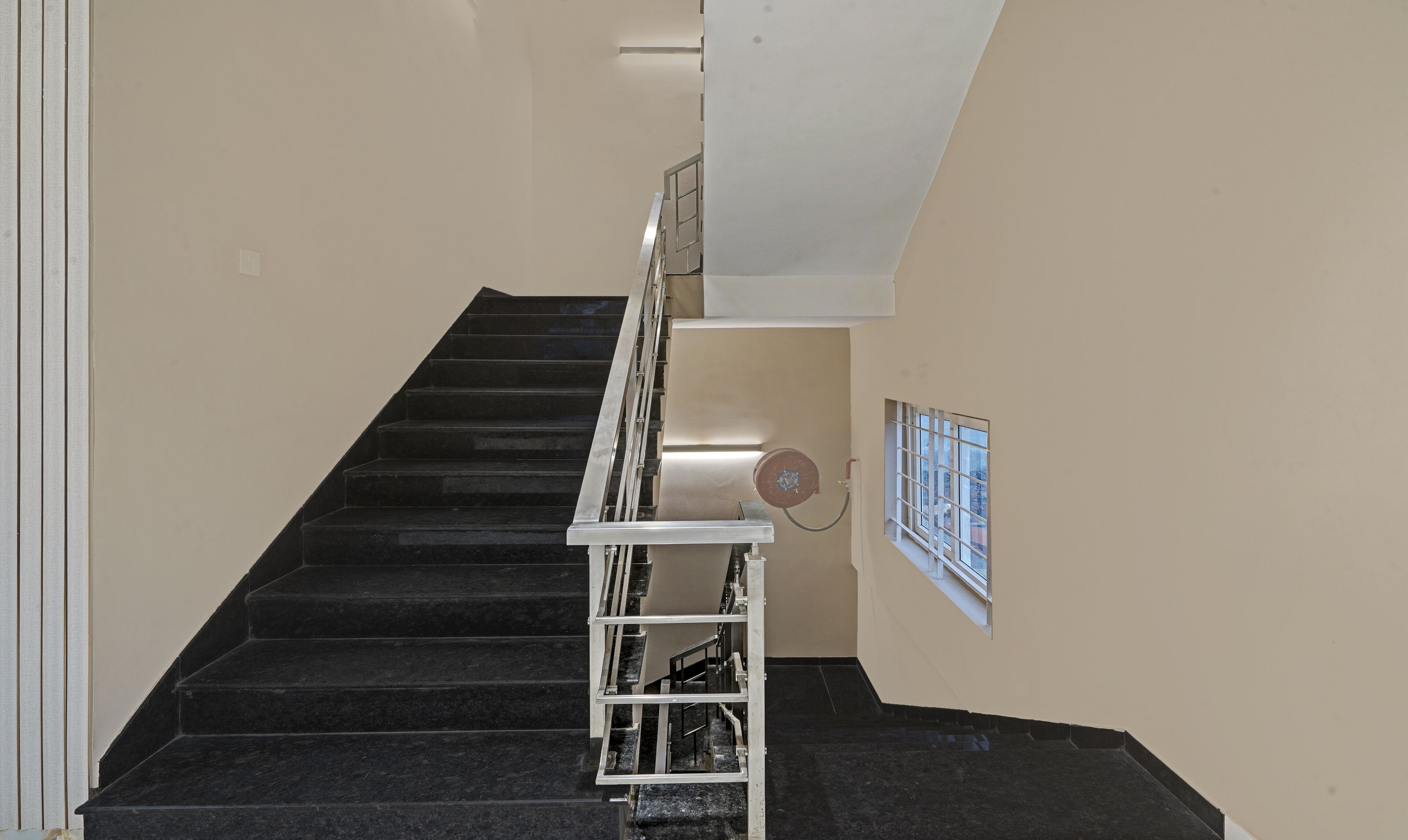 A staircase with a handrail, a window with bars, and a wall-mounted device.