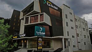 Un hotel de varios pisos con un diseño moderno, que presenta un letrero llamativo para 'Hotel La Orchid' y 'Uma Mess'.