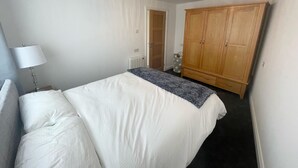 A bedroom with a bed, a wardrobe, a radiator, and a lamp. - Beautiful Private Detached 1-bed Bungalow (Penarth)