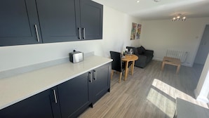 A modern kitchen with dark cabinets, a countertop, and a dining area with a table and chairs. - Beautiful Private Detached 1-bed Bungalow (Penarth)