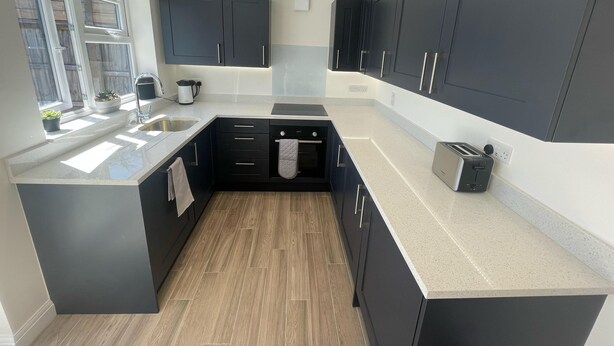 A modern kitchen with dark cabinets, a countertop, and a built-in oven. - Beautiful Private Detached 1-bed Bungalow (Penarth)