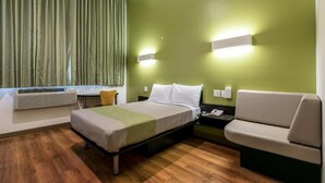 A hotel room with a bed, a chair, a desk, and a window with curtains. - The Feather Factory (Long Island City)