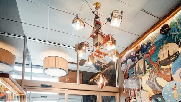 A bookstore with a variety of bookshelves, a unique ceiling light fixture, and a large window with a view of the street. - The Feather Factory (Long Island City)