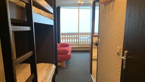 Ein schmaler Korridor mit Etagenbetten an einer Seite und einer Tür, die auf einen Balkon mit Geländer führt.