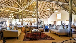 A spacious living area with high ceilings and exposed wooden beams, furnished with sofas and a coffee table, and decorated with wall art and rugs. - Kwantu Game Reserve (Gqeberha (Port Elizabeth))