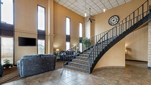 Un vaste espace de vie agrémenté d’un escalier en colimaçon, d’une grande horloge murale et d’un téléviseur à écran plat fixé au-dessus d’un coin salon.