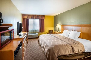 Habitación de hotel con cama, escritorio, computadora, televisor y ventana con cortinas.