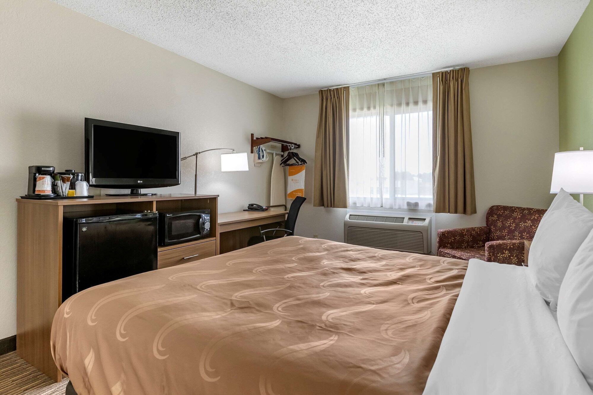 A hotel room with a bed, a desk with a computer, a television, a microwave, and a coffee maker.