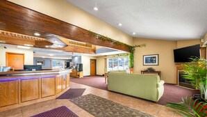 Un hall d’hôtel avec un comptoir d’accueil, un canapé vert, un téléviseur et une grande fenêtre.