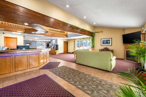 A hotel lobby with a reception desk, a green sofa, a TV, and a large window. - Rodeway Inn Milaca (Milaca)