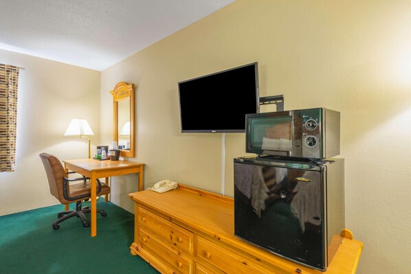 A hotel room with a desk, chair, television, refrigerator, and a mirror.