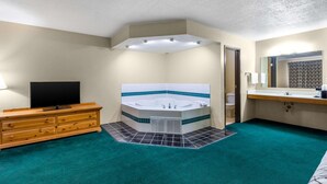 Une salle de bain avec une baignoire, un meuble-lavabo et un téléviseur posé sur une commode.