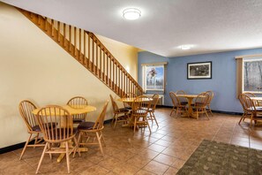 A dining area with wooden chairs and tables, a staircase, and a window with a view. - Rodeway Inn Milaca (Milaca)