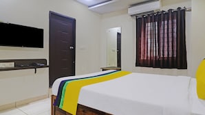 Ein Hotelzimmer mit einem Bett, einem flachbildfernseher an der Wand, einer Tür und einem mit Vorhängen versehenen Fenster.