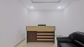 Ein Empfangsschalter mit Holzbeschlag und dunklem Holzfuß, eine schwarze Ledersofa und ein gefliestes Parkett.