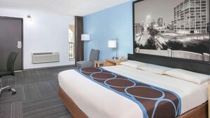 Hotellihuone, jossa on suuri sänky, työpöytä, tuoli, lamppu ja näkymä kaupunkiin.