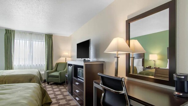 Een hotelkamer met twee bedden, een bureau met een computer, een stoel, een televisie en een koffiezetapparaat.