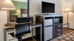 Een hotelkamer met een bureau, een stoel, een televisie, een magnetron en een koelkast.