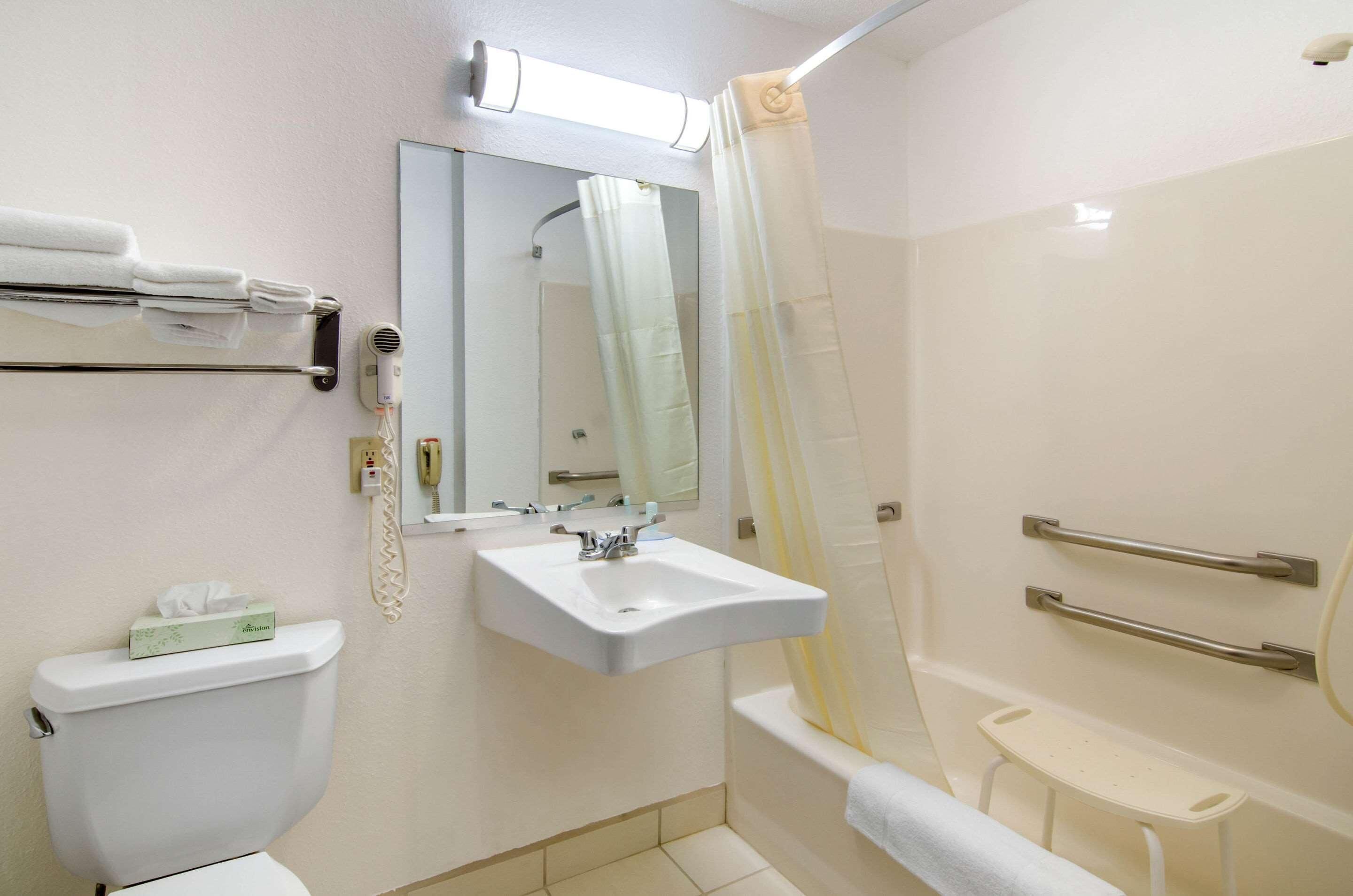 A bathroom with a toilet, sink, mirror, towel rack, shower curtain, and grab bars.