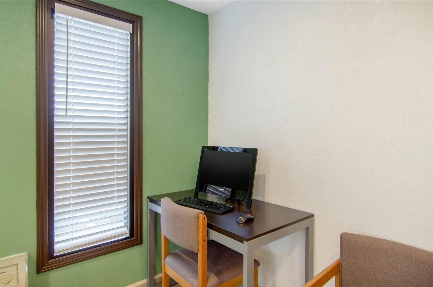 A room with a desk, a computer, and a window with blinds.