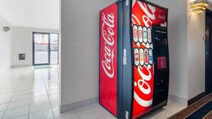 A Coca-Cola vending machine in a hallway with a tiled floor and a door in the background. - Quality Inn Russell, KS (Russell)