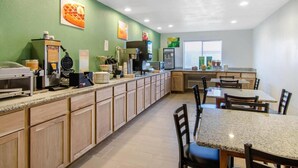 A kitchen with a long counter, various appliances, and a dining area with tables and chairs. - Quality Inn Russell, KS (Russell)
