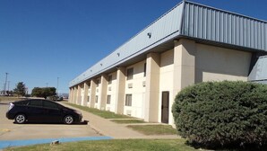 Une rangée de chambres d’un motel, toutes de plain-pied, avec un parking et un arbuste vert devant.