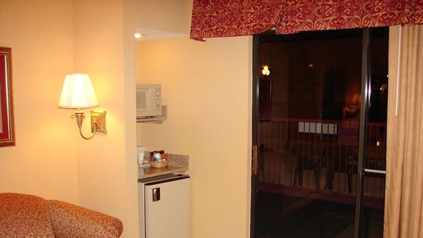 Une chambre d’hôtel équipée d’un canapé, d’une petite kitchenette, d’une porte-fenêtre coulissante donnant sur un balcon et d’une lampe fixée au mur.
