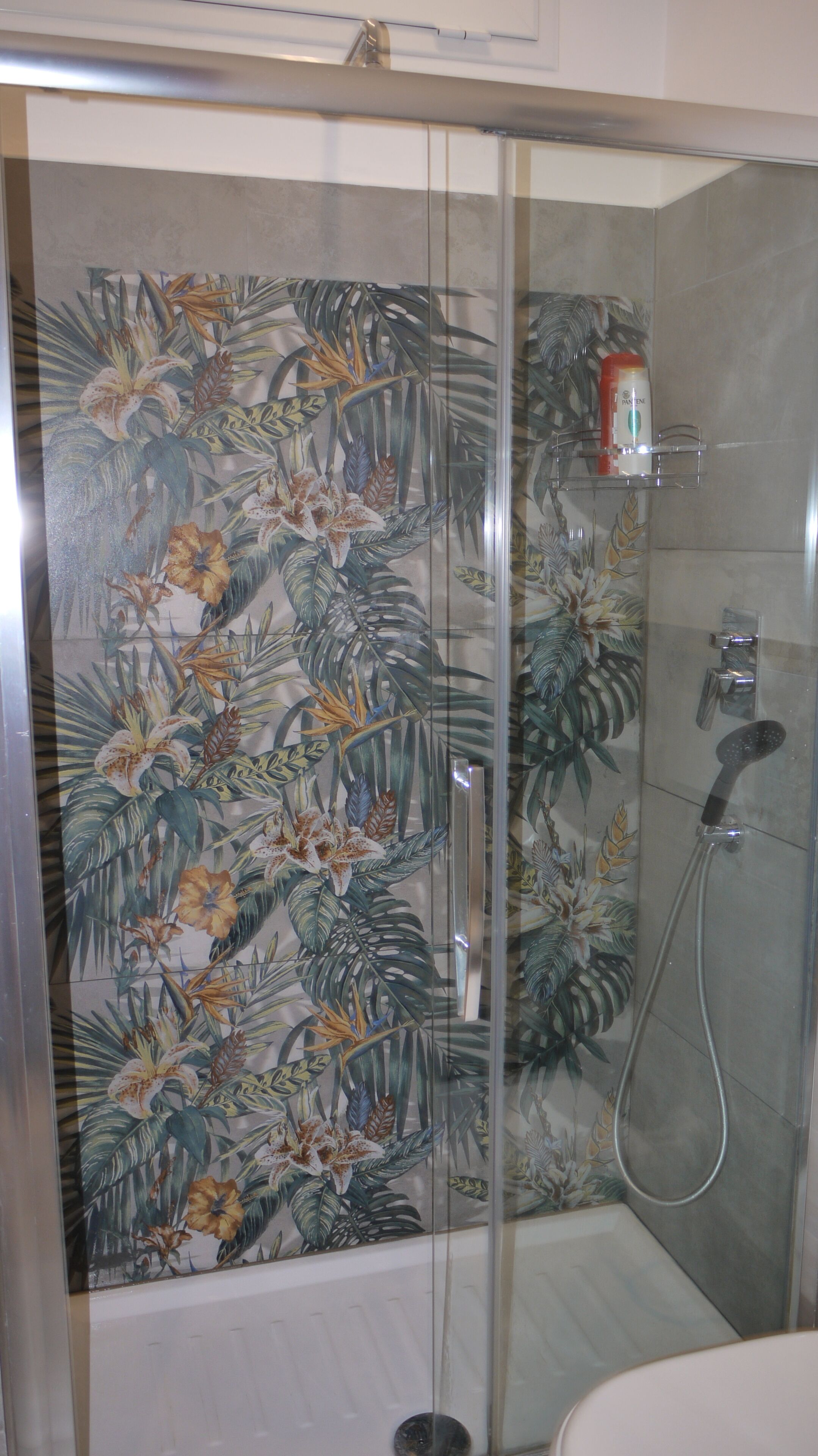 A shower with a glass door, a handheld showerhead, and a soap dispenser on a shelf.