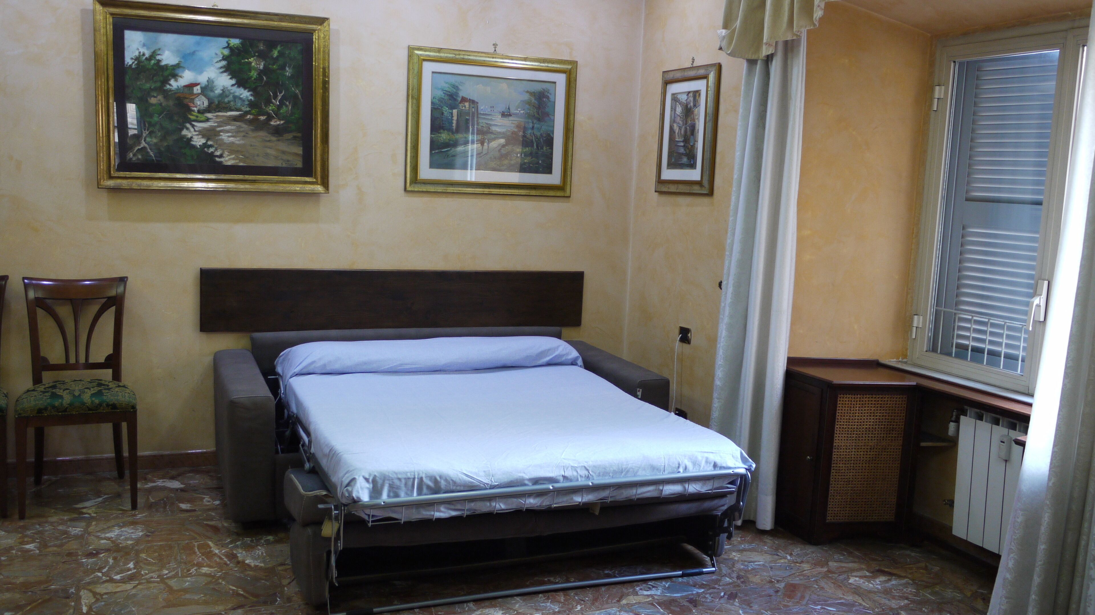 A bedroom with a bed, a chair, and three framed pictures on the wall.