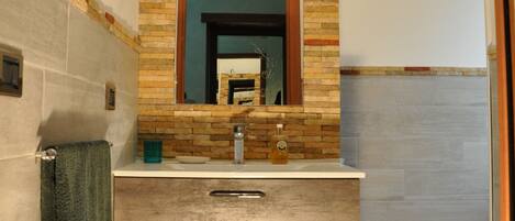 A bathroom with a wooden vanity, a mirror, and a tiled shower area.
