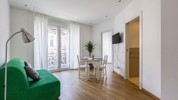 A room with a green sofa, a dining table with chairs, a potted plant, and a TV mounted on the wall. - The apartment is located in a stunning location, almost impossible to find! You are in the authentic heart of Milan, between Sant'Ambrogio district, renowned above all for the church of Santa Maria delle Grazie and the Catholic University and the charm o (Milano)