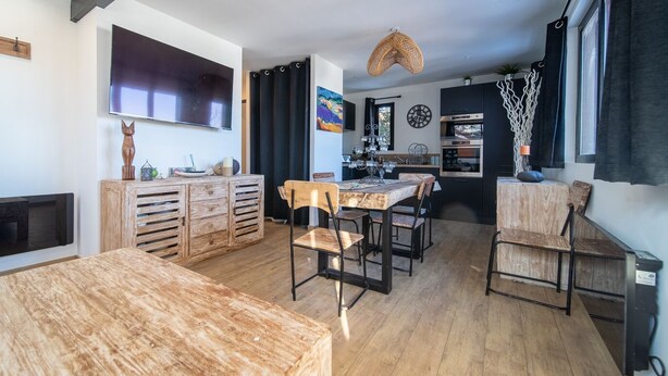 Una cocina moderna con armarios de madera, un comedor con mesa y sillas de madera, y un televisor montado en la pared.