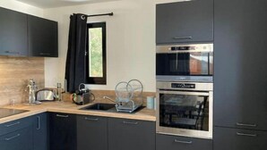 Una cocina moderna con armarios oscuros, horno empotrado y ventana con cortinas negras.