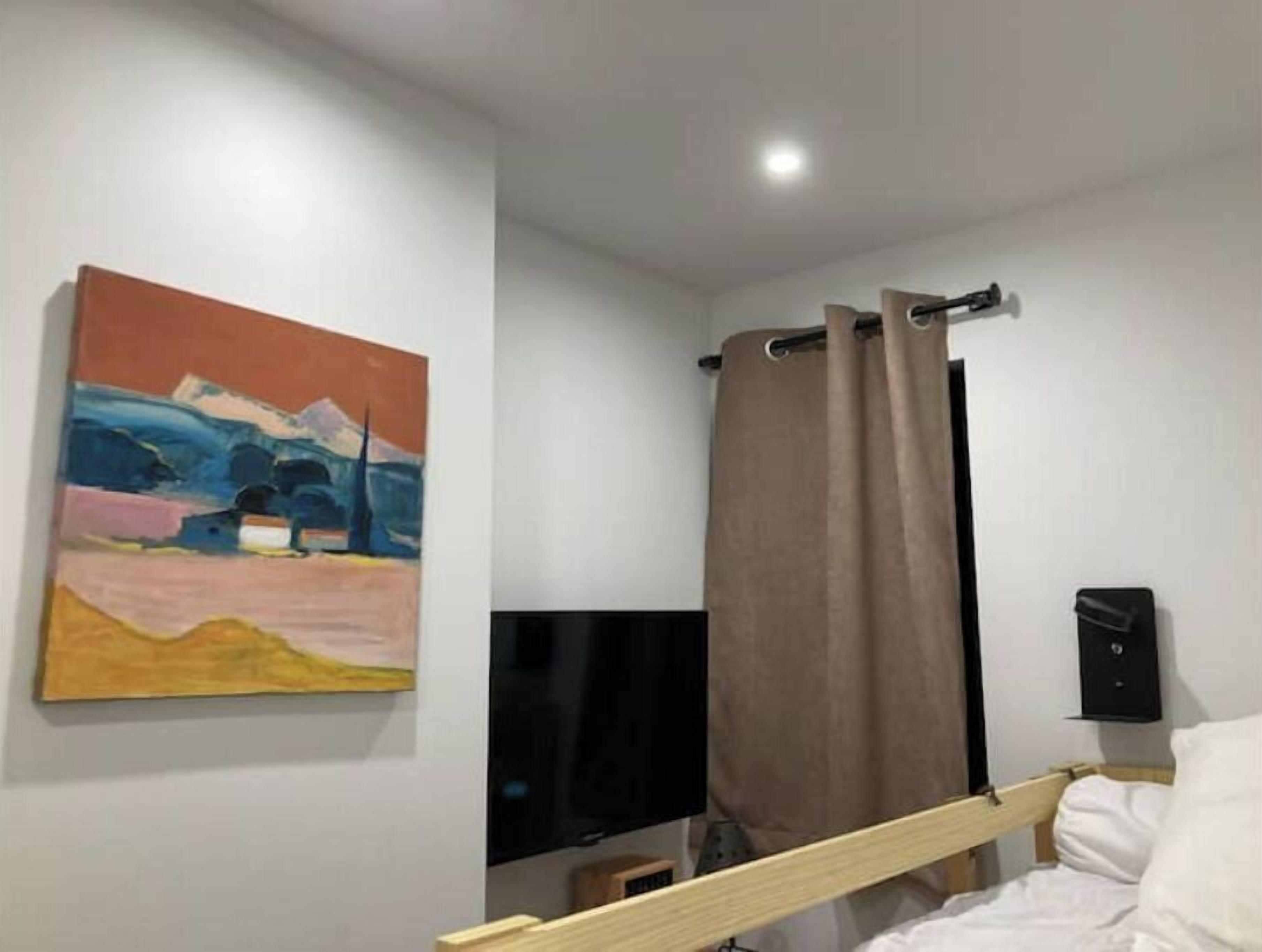 Une chambre à coucher avec un lit, un téléviseur à écran plat, un tableau au mur et un rideau.