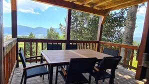 A wooden deck with a table and chairs, overlooking a scenic landscape with trees and mountains. - Bel Appartement Dans un Chalet vue sur le lac (Les Angles)