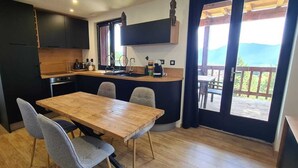 A compact kitchen with a wooden table and chairs, a built-in oven, and a window overlooking a deck. - Bel Appartement Dans un Chalet vue sur le lac (Les Angles)